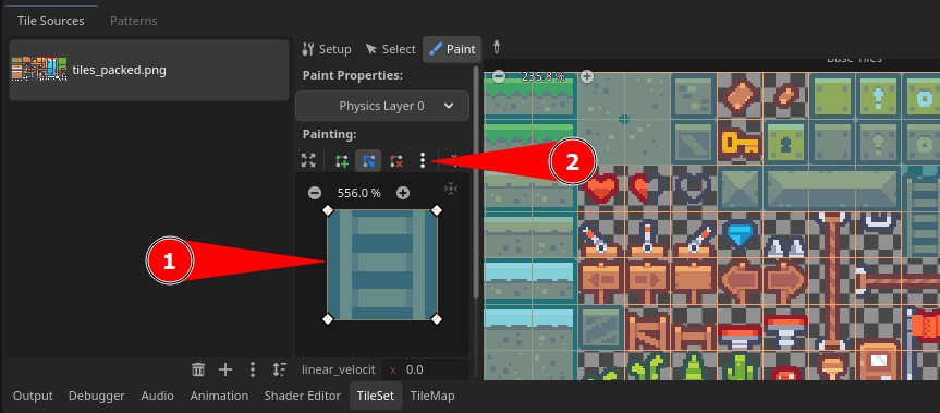 A l'editor TileSet de Godot, amb la pestanya "Pintura" activa, l'usuari està assignant propietats de col·lisió a les fitxes: la secció "Pintura" mostra "Capa física 0" seleccionada al menú desplegable de l'editor de propietats (indicat per la fletxa vermella 2), i actualment es selecciona una rajola de ratlles blaves per pintar (resaltada per la fletxa vermella 1); la font de mosaic "tiles_packed.png" és visible al tauler Fonts de mosaic de l'esquerra, mentre que el costat dret mostra la graella de l'atles de fitxes amb diversos actius del joc, com ara cors, claus i plataformes, preparats per a l'assignació de col·lisions.
