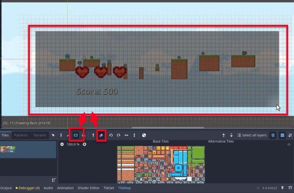 A la interfície d'edició de TileMap de l'editor de Godot, l'usuari està modificant la disposició de "level_2(*)" seleccionant eines per editar el mapa de mosaic: l'eina rectangle amb contorn vermell (per seleccionar o esborrar regions rectangulars) i l'eina llapis (per col·locar fitxes) es destaquen a la barra d'eines sota la finestra gràfica; la finestra mostra un nivell d'art de píxels amb temàtica del desert amb plataformes, monedes, enemics, tres icones de cor i una etiqueta "Puntuació: 500", superposada amb una quadrícula i un rectangle de selecció vermell que indica l'àrea de dibuix actual (61x19 fitxes a la posició 52,11); el tauler TileMap a la part inferior mostra les fitxes de temàtica del desert disponibles a "Rajoles base" i "Rajoles alternatives", confirmant que l'usuari està substituint les fitxes del bosc originals per actius del desert com a part de la creació d'un disseny únic de nivell 2.